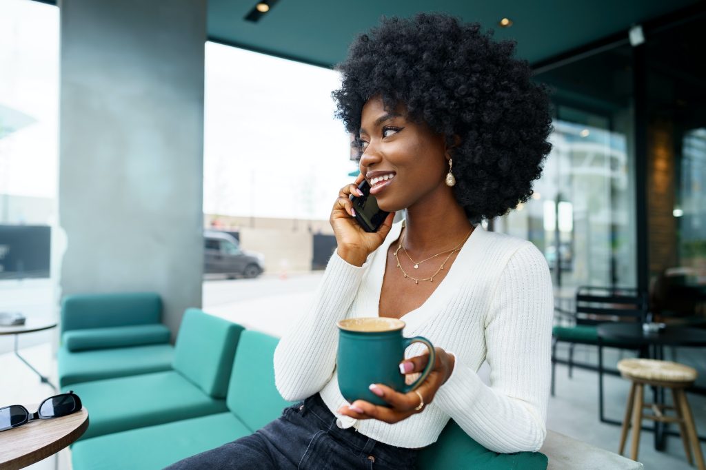 Smiling young african woman talking on cellphone at cafe